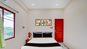 A bedroom with a bed, a window, a red door, and three framed artworks on the wall.