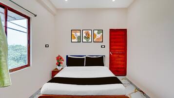 A bedroom with a bed, a window, a red door, and three framed artworks on the wall.
