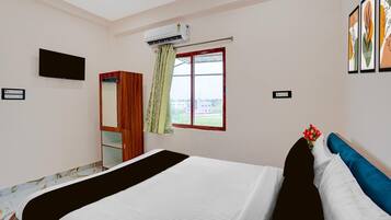 Hotelkamer met een bed, een kledingkast, een televisie, een airconditioningapparaat, een raam met gordijnen en lijstwerken aan de muur.