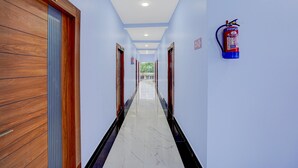 Un couloir d’hôtel avec des portes en bois, un extincteur fixé au mur et un panneau indiquant le numéro de la chambre.