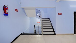 Un escalier avec une signalisation indiquant la sortie de secours, un extincteur et une main courante en métal.