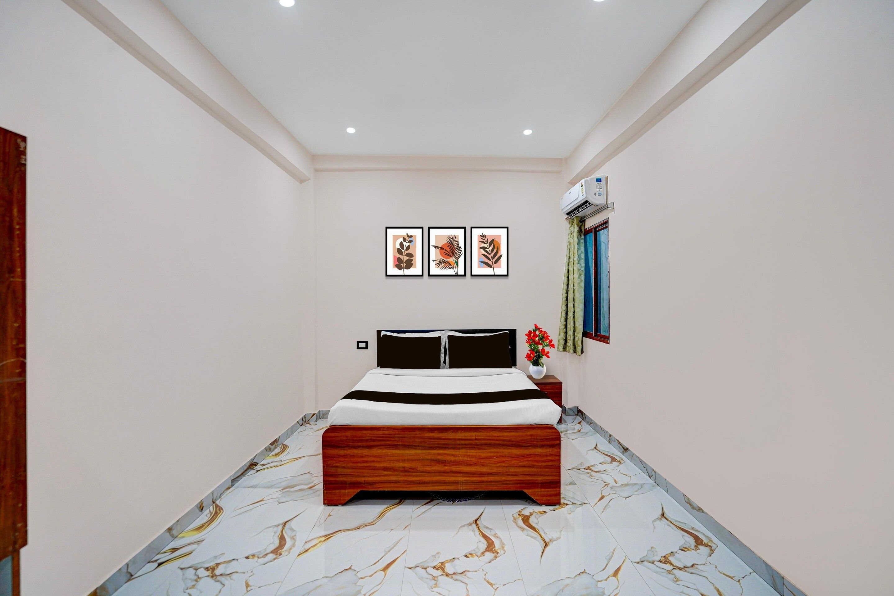 A bedroom with a bed, a nightstand, a wall-mounted air conditioner, and framed artwork on the wall.