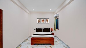 A bedroom with a bed, a nightstand, a wall-mounted air conditioner, and framed artwork on the wall.