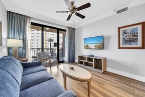 Ein modernes Wohnzimmer mit einer Couch, einem Couchtisch, einem Fernseher und einem Balkon mit Blick auf Gebäude und Palmen.