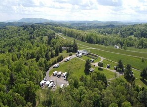 An aerial view of a campground with RVs parked in designated areas, surrounded by dense forest and open fields. - Couple's Getaway Camping Cabin with 5-Bathroom Bath House Nearby, Pets Welcome (Fancy Gap)