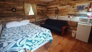 Een kamer met een bed, een bank, een magnetron en een houten wand.