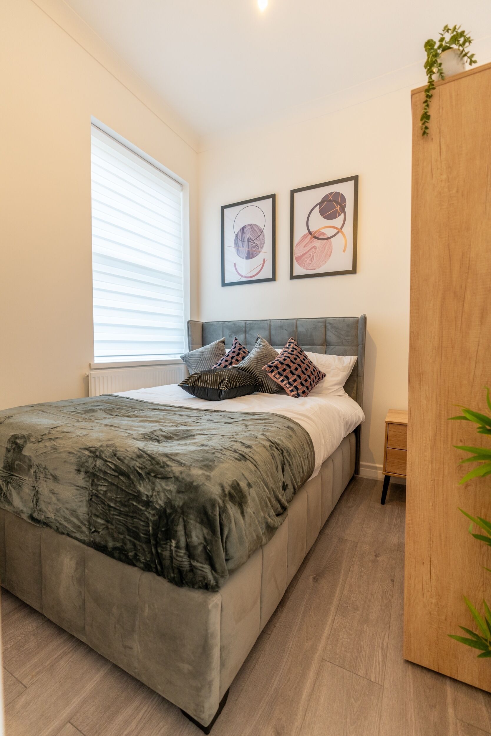 A modern bedroom with a large bed, a wooden wardrobe, and two framed artworks on the wall.