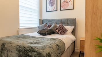 A modern bedroom with a large bed, a wooden wardrobe, and two framed artworks on the wall.