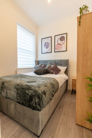 A modern bedroom with a large bed, a wooden wardrobe, and two framed artworks on the wall. - Modern Flat in Waterloo (London)