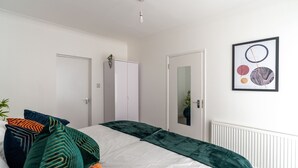 Een slaapkamer met een bed, kussens, een radiator en een ingelijst foto aan de muur.