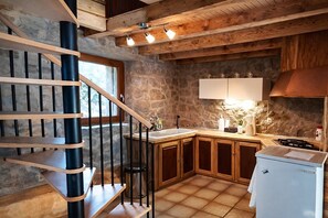 Une cuisine avec un mur en pierre, des meubles de rangement en bois, un réfrigérateur blanc et un escalier en bois.