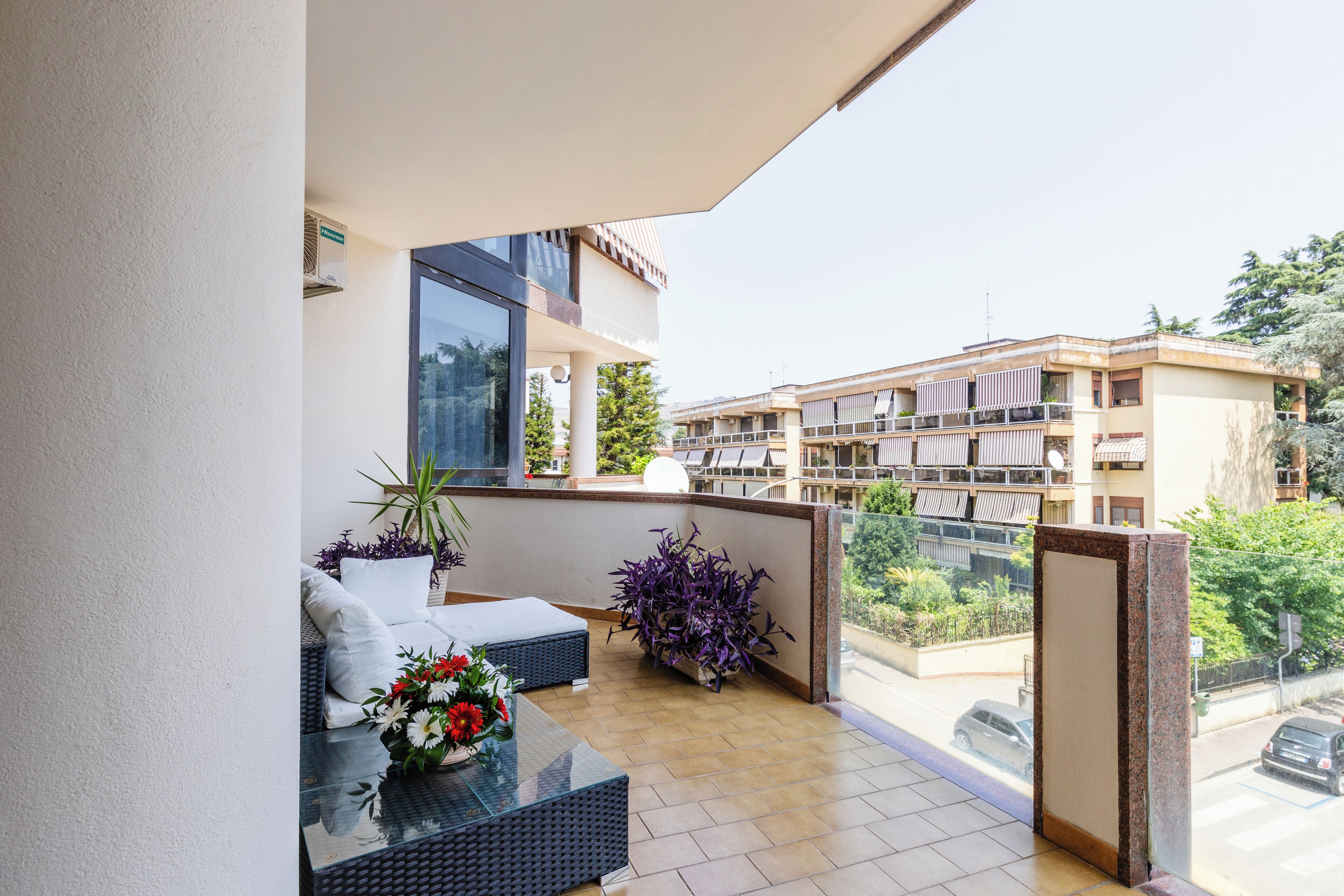 A balcony with a sofa, a glass table, and potted plants.
