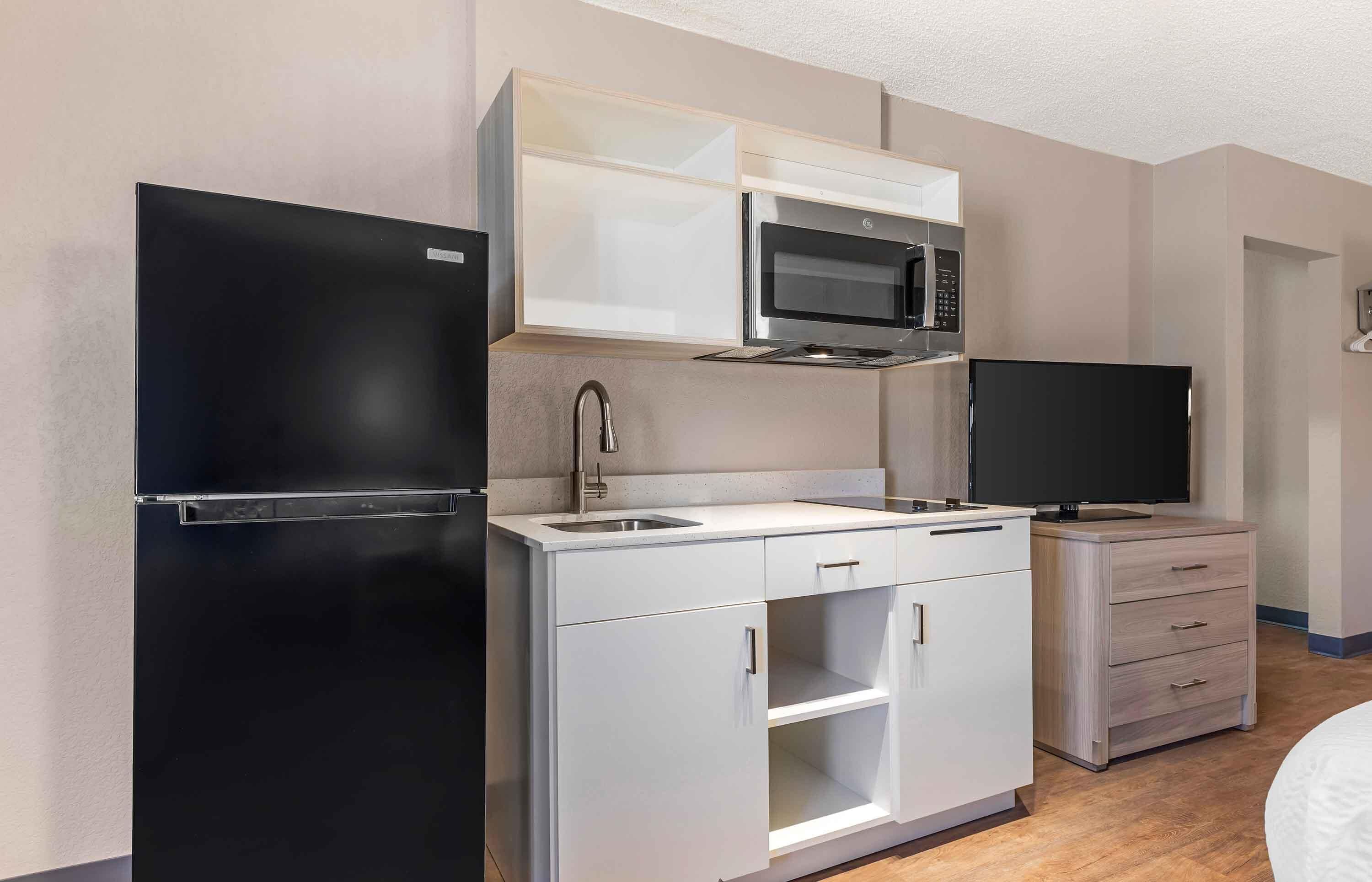 Una kitchenette compacta con un refrigerador negro, un microondas, un fregadero y un televisor.