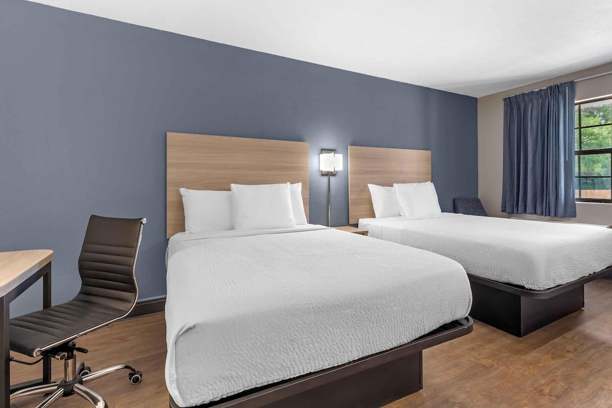 A hotel room with two beds, a desk, a chair, and a window with curtains.