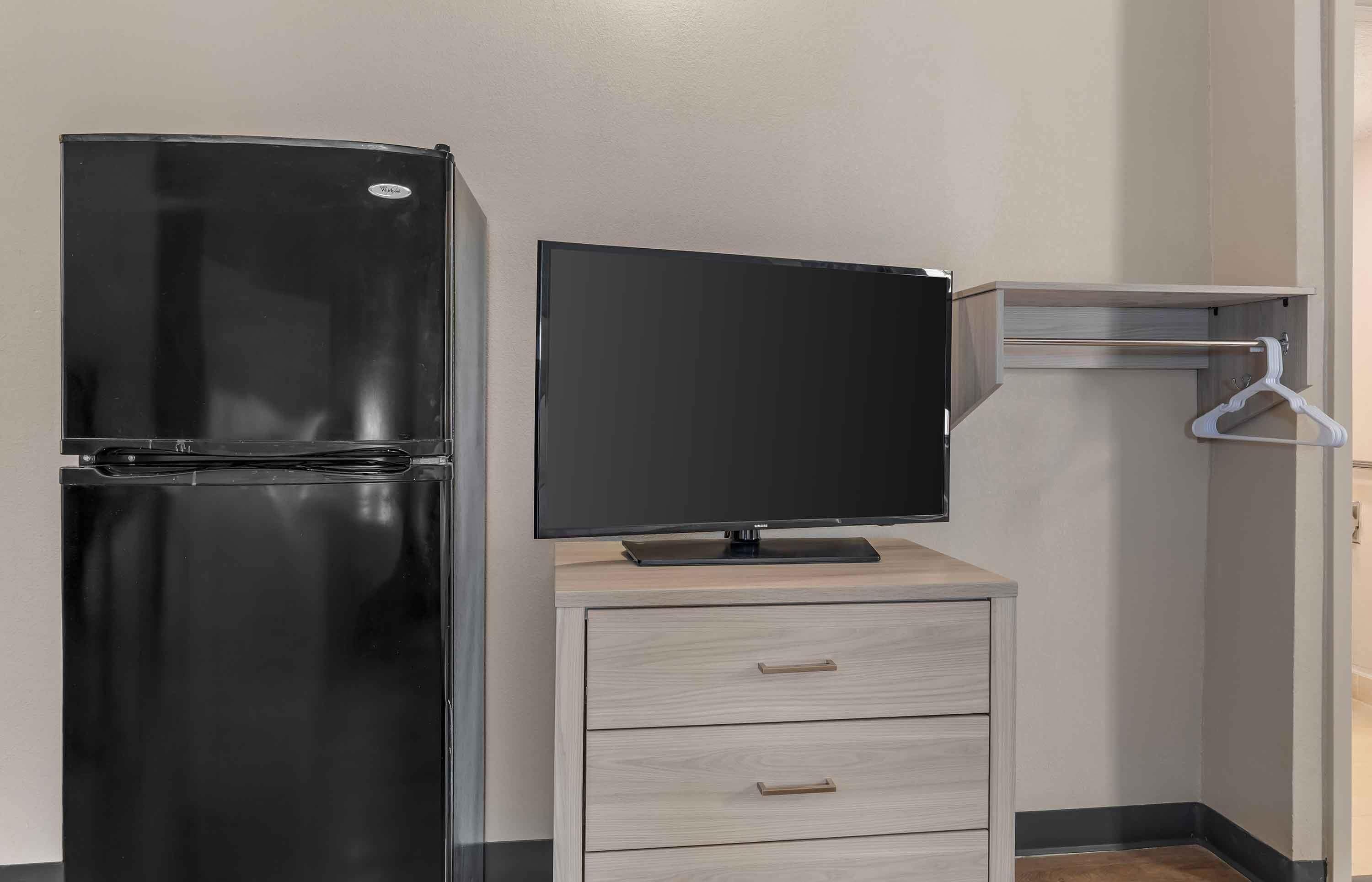 Una kitchenette con un refrigerador negro, un televisor de pantalla plana y un mueble de madera con un perchero.