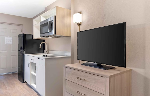 A compact kitchen with a microwave, refrigerator, and a flat-screen TV on a wooden cabinet.