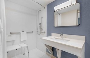 A modern bathroom with a walk-in shower, a sink with a mirror, and a toilet with a grab bar.