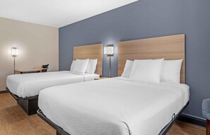 A hotel room with two beds, a desk, and two wall-mounted lamps.