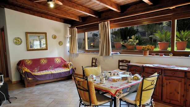 A cozy room with a wooden ceiling, a sofa, a dining table with chairs, and a window with potted plants. - Marta's Studio in Formia (Formia)
