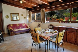 Une pièce chaleureuse avec un plafond en bois, un canapé, une table à manger avec des chaises et une fenêtre agrémentée de plantes en pot.