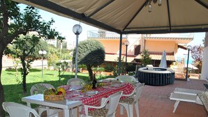 An outdoor patio with a table set for dining, surrounded by white chairs with floral cushions, a small garden, and a hot tub. - Marta's Studio in Formia (Formia)