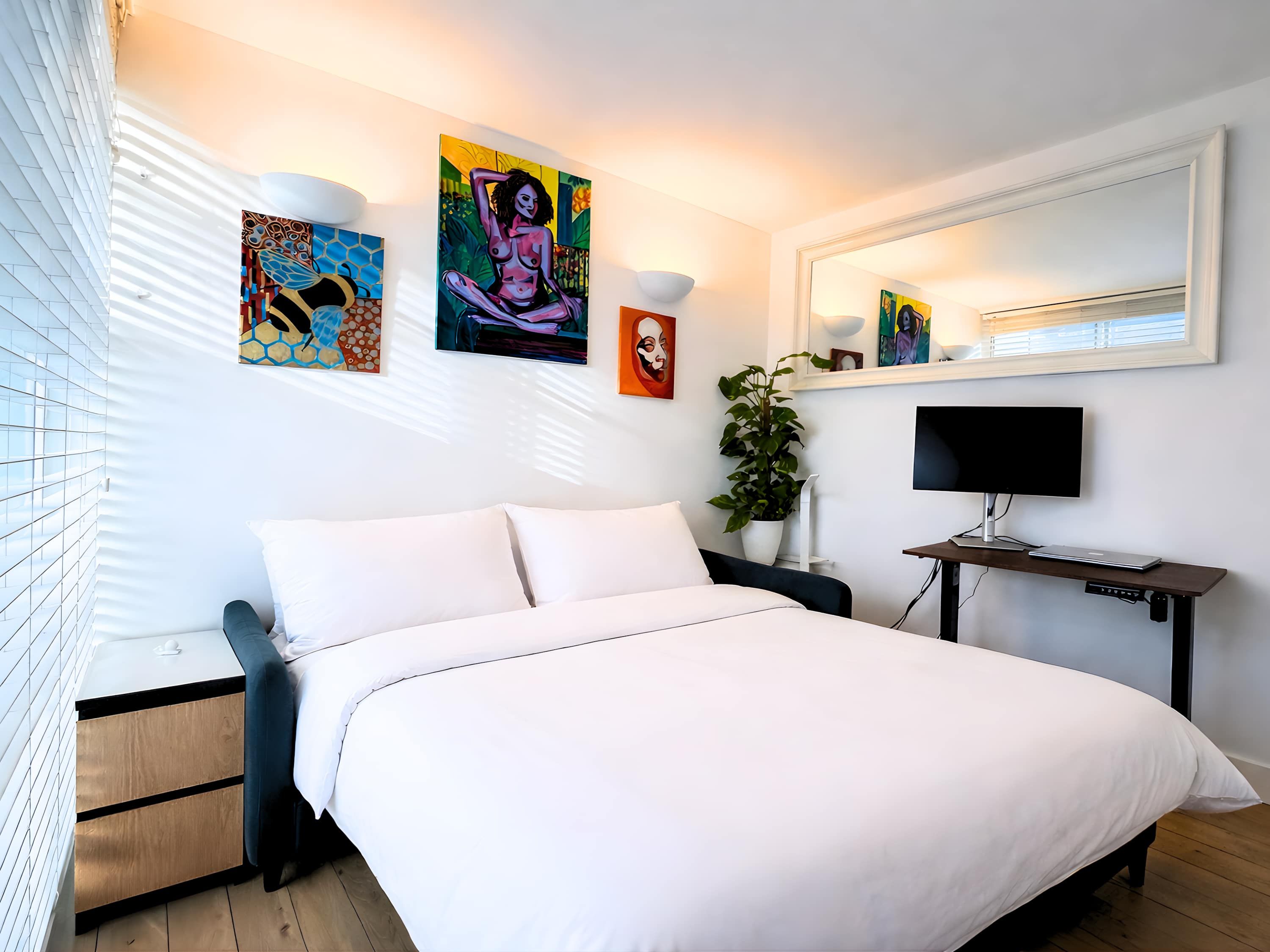 Une chambre à coucher moderne, dotée d’un grand lit, d’un bureau avec un ordinateur et d’œuvres d’art accrochées aux murs.