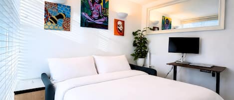 Une chambre à coucher moderne, dotée d’un grand lit, d’un bureau avec un ordinateur et d’œuvres d’art accrochées aux murs.
