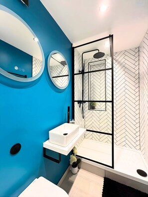 Ein modernes Badezimmer mit blauer Wand, Waschbecken in Weiß, einem Spiegel und einer Duschkabine.