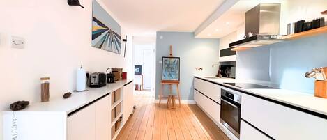 A modern kitchen with white cabinetry, a wooden floor, and a painting on the wall.