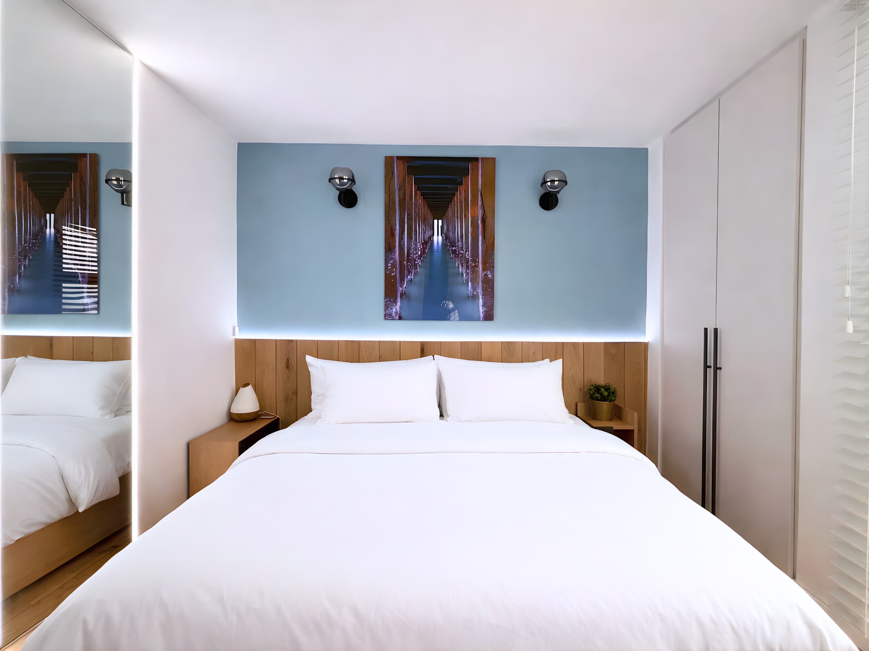 Une chambre d’hôtel moderne avec un grand lit, une table de chevet, une lampe fixée au mur et un tableau au-dessus du lit.