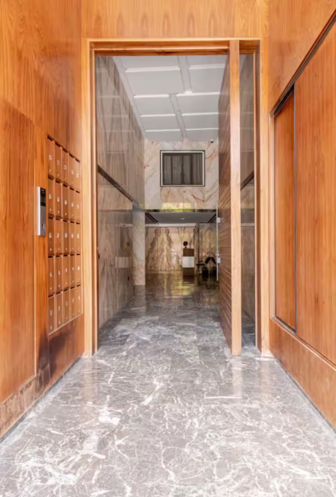 A hallway with wooden lockers on one side and a marble floor.