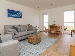 A modern living room with a grey sofa, a woven ottoman, and a dining area with a wooden table and chairs. - The Lookout (Scarborough)