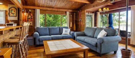 Interior de una cabaña con piso de madera, un conjunto de sofás, una mesa de comedor y una zona de bar.