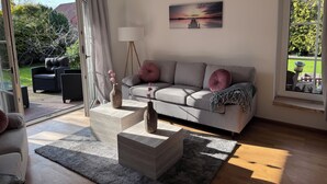 Een moderne woonkamer met een grijze bank, twee bijzettafels, een vloerlamp en een schilderij van een zonsondergang.