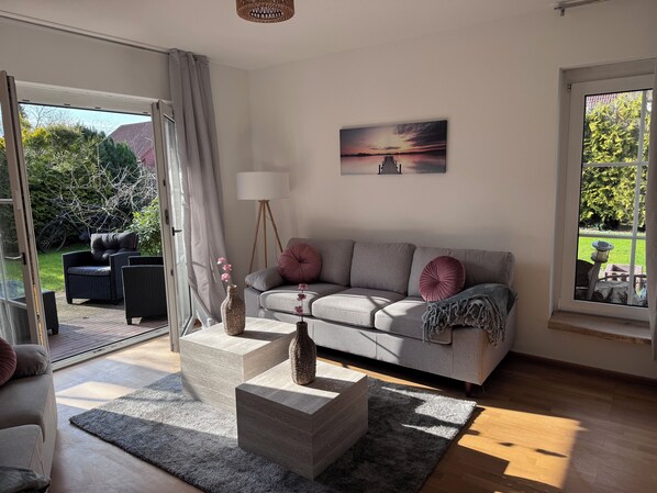 A modern living room with a grey sofa, two side tables, a floor lamp, and a painting of a sunset. - Cozy, rustic house with a fireplace, large garden, and 2 bathrooms for up to 6 people (Schüttorf)