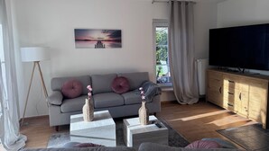Een moderne woonkamer met een grijze bank, een flatscreen televisie en een houten kast.