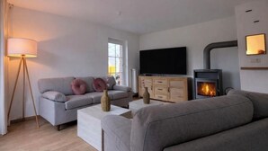 Een woonkamer met een bank, een salontafel, een televisie en een houtkachel.