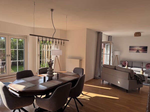 A dining area with a table, chairs, and a lamp. There is a sofa and a lamp in the living area.