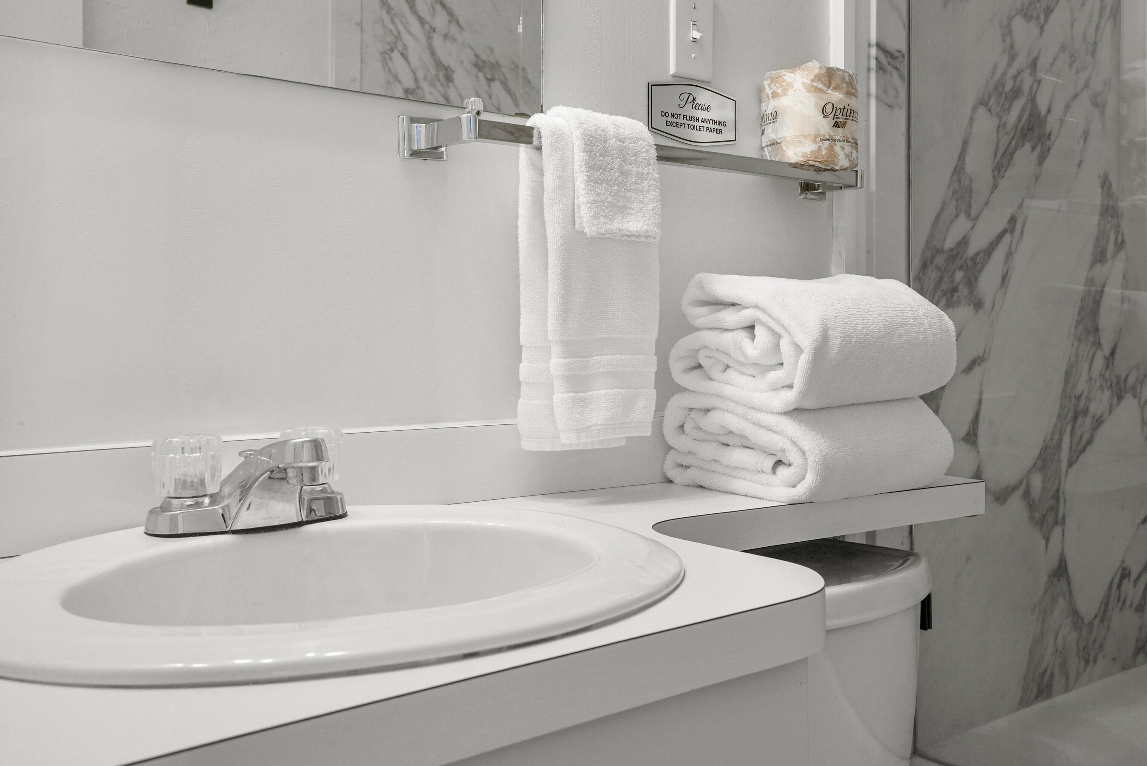 A bathroom with a white sink, a towel rack with folded towels, and a sign above the rack.