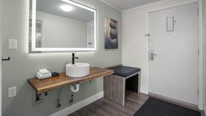 Une salle de bain avec un lavabo blanc, un meuble-lavabo en bois, un miroir avec éclairage à DEL, un porte-serviettes et une porte avec une serrure.