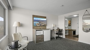 Une chambre d’hôtel équipée d’un bureau, d’une chaise, d’un four à micro-ondes et ornée d’un tableau représentant un paysage côtier.