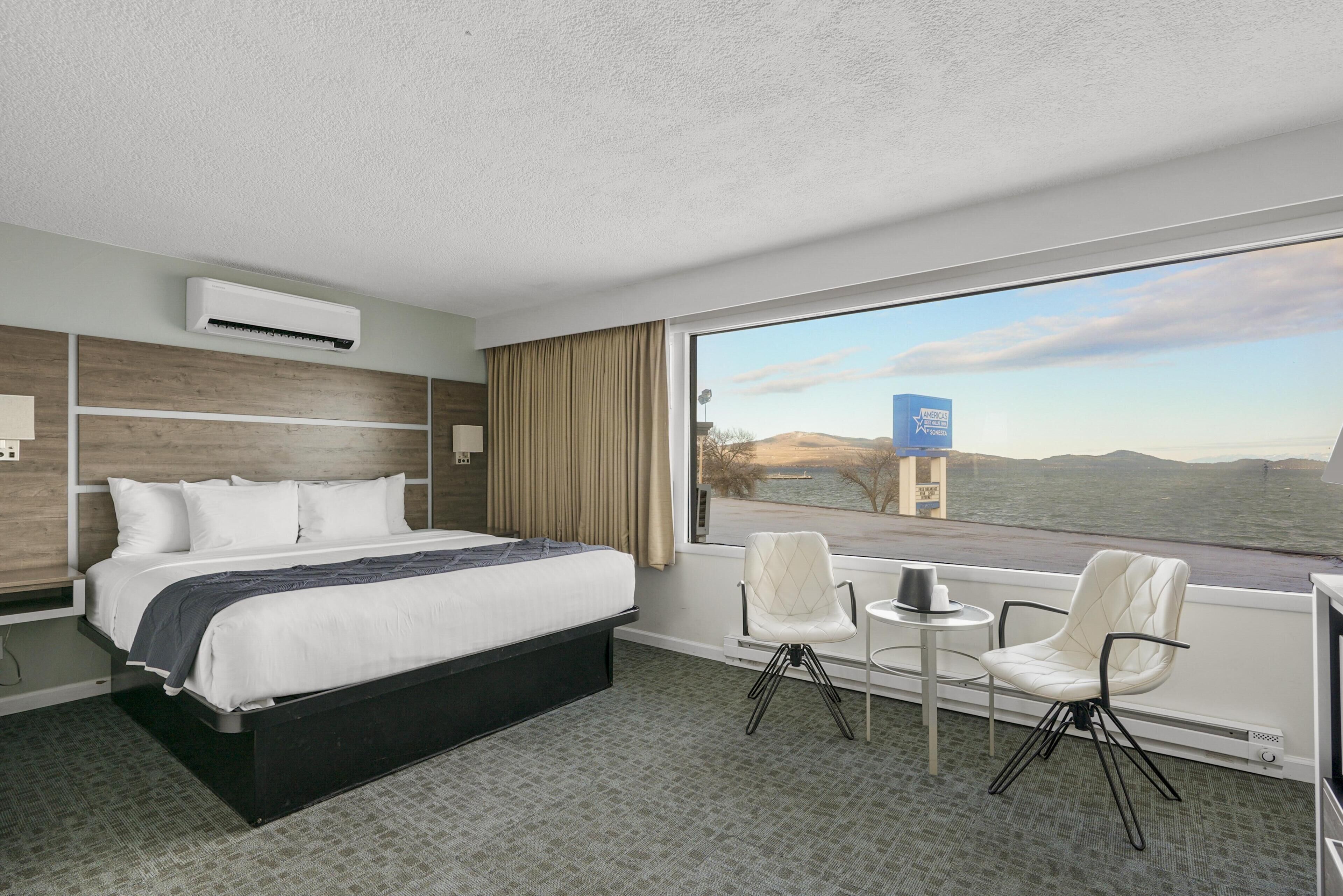 A hotel room with a bed, two chairs, a small table, and a view of the sea.