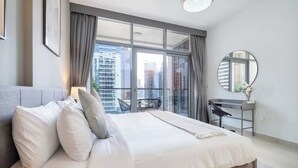 Ein modernes Hotelzimmer mit einem großen Bett, einem Schreibtisch und Blick auf die Stadt durch raumhohe Fenster.