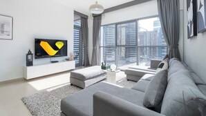 Ein modernes Wohnzimmer mit einem grauen Sofa, einem Flachbildfernseher und einem großen Fenster mit Blick auf die Stadt.
