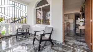 A modern interior with two dark wooden chairs, a marble floor, and a view of a balcony with a railing.