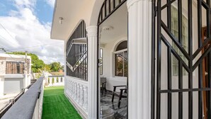 A covered outdoor area with a green artificial turf, white columns, and black metal gates.