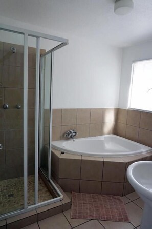 Un baño con mampara de vidrio, bañera y lavamanos.