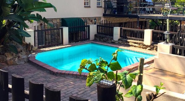Una piscina rectangular con borde de ladrillo, rodeada por un muro de piedra y una valla metálica.