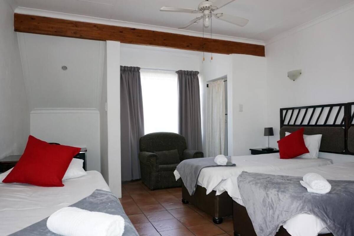 Habitación de hotel con dos camas, una silla, un ventilador de techo y vistas a través de un umbral.