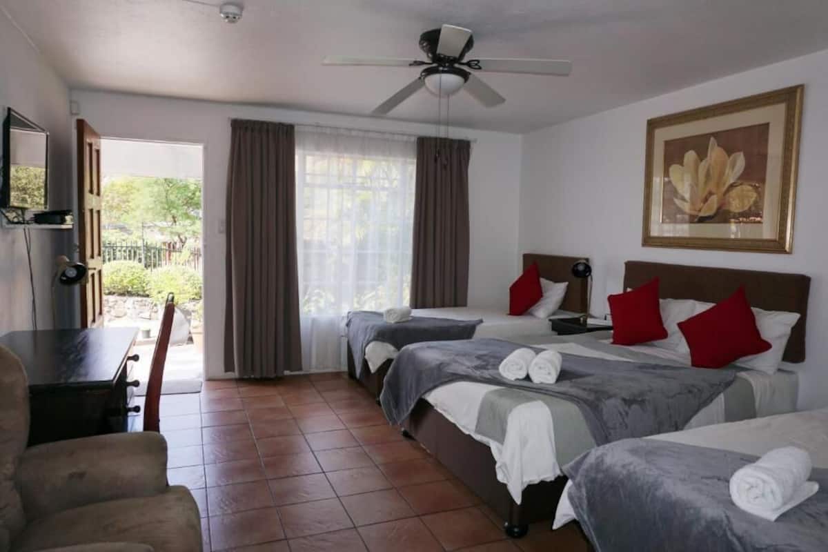 Habitación de hotel con dos camas, un escritorio, una silla, un ventilador de techo y una ventana con cortinas.